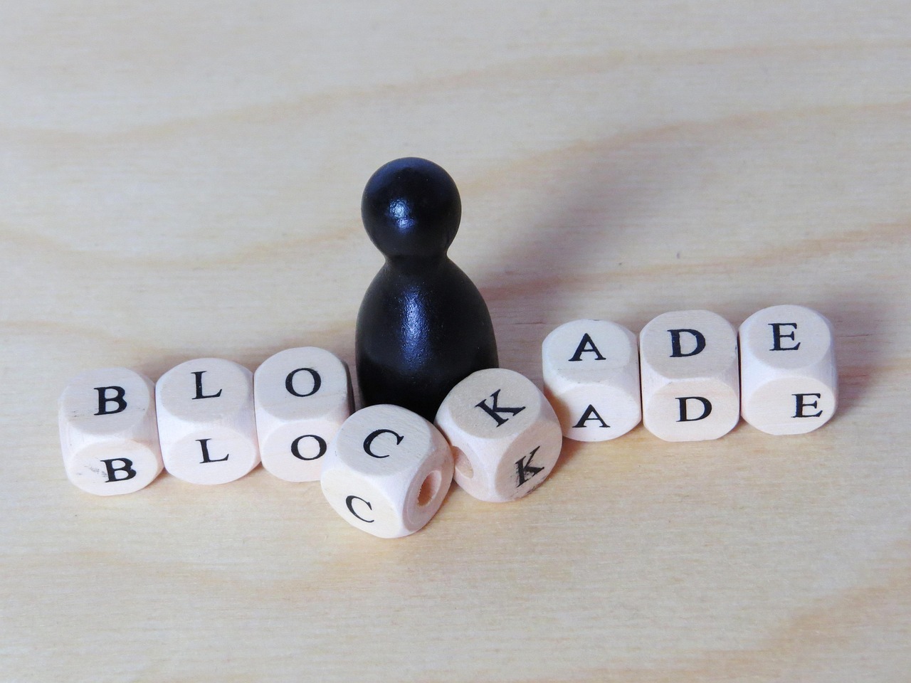 Holzwürfel mit dem Wort Blockade und eine schwarze Spielfigur